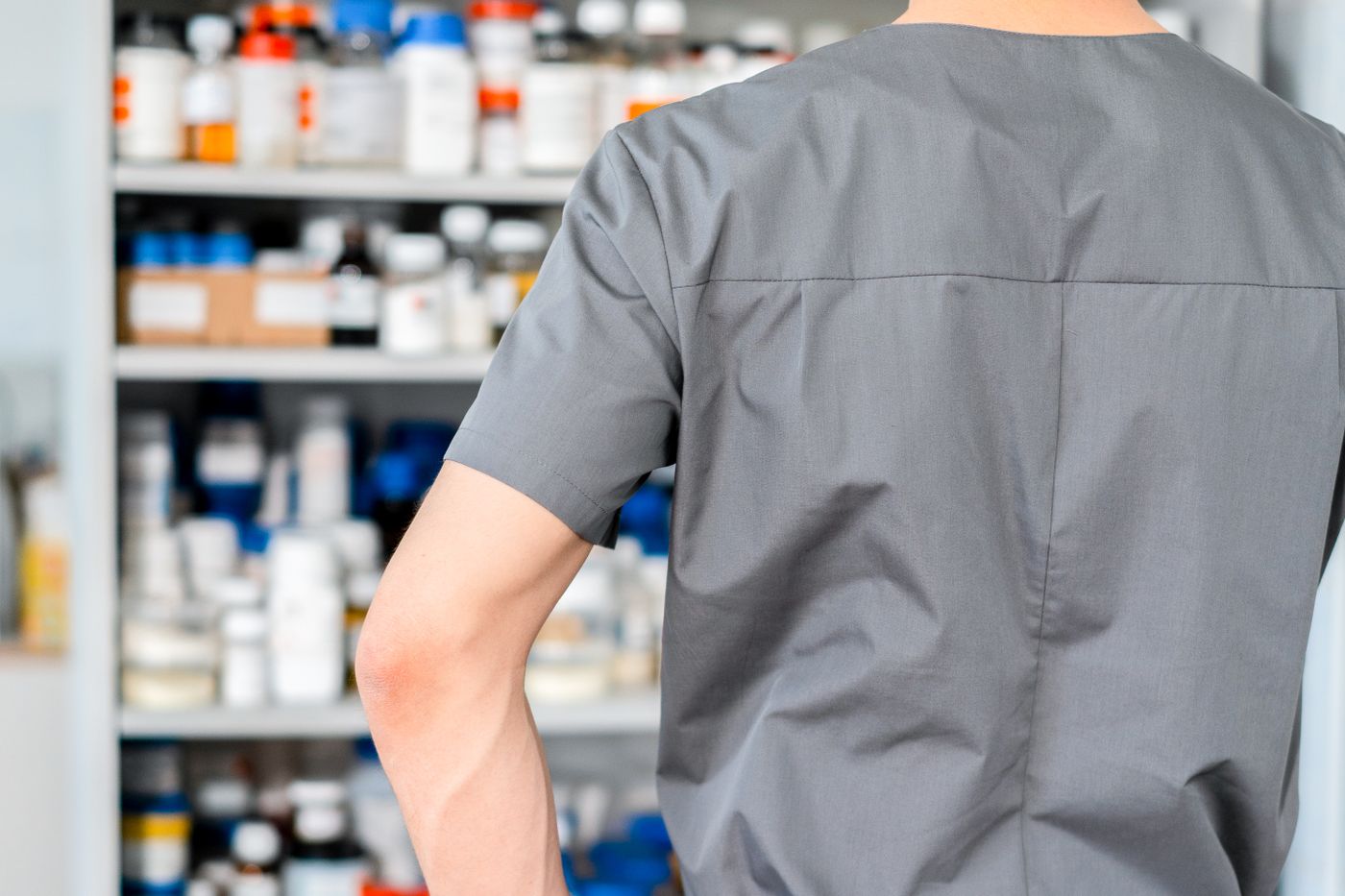 A pharmacist facing a dispensary cabinet stocked with medication