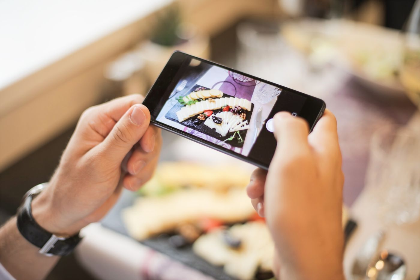 A person photographing a plated dish on a smartphone in a restaurant